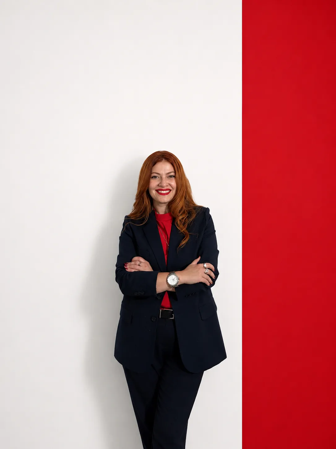 Oksana Nasadiuk smiling with her arms crossed, beside a red wall